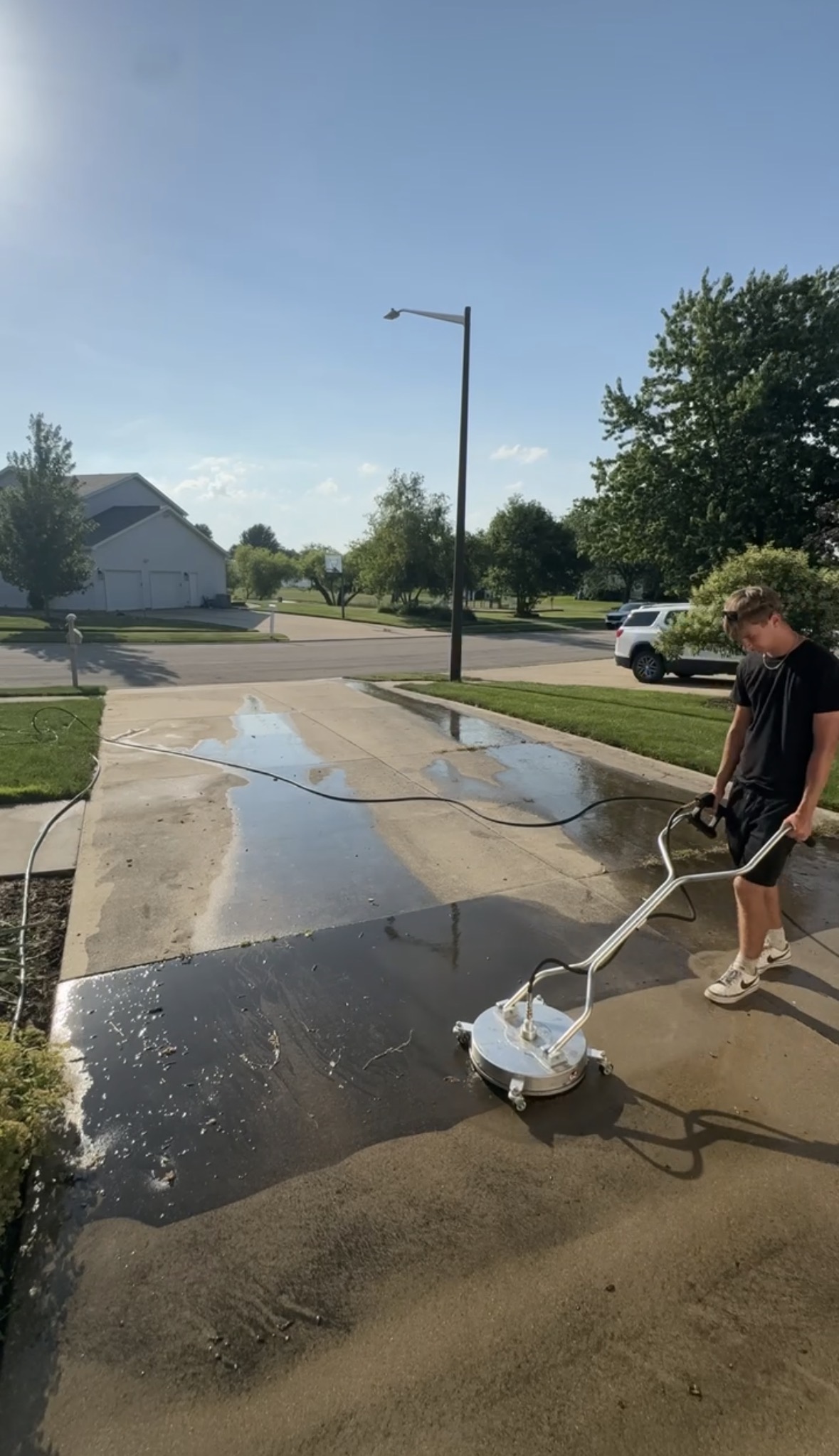 Prime Shine crew member cleaning a residential concrete driveway with a surface cleaner